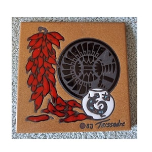 May include: Square ceramic tile with a brown background featuring a design of red chili peppers, a dark gray circular pattern, and a small white vase with a black and blue design. The text "83 Teissedre" is printed on the bottom.