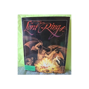 Könnte beinhalten: Ein Vintage-Exemplar von J.R.R. Tolkiens Buch "Der Herr der Ringe, Band 1". Das Cover zeigt eine Fantasy-Illustration einer geflügelten Kreatur, die gegen eine Figur in der Nähe eines Feuers kämpft. Der Titel ist in einer stilisierten Schrift auf dunklem Hintergrund.