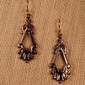 May include: A pair of gold-toned dangle earrings with a detailed, ornate design. The earrings feature a teardrop shape with a fan-like design at the bottom.