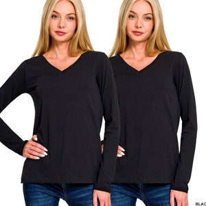 May include: Two black long-sleeve V-neck shirts. The shirts are made of a soft material and have a classic design. The shirts are shown on a model with blonde hair and blue jeans. The word "BLACK" is printed in the bottom right corner.