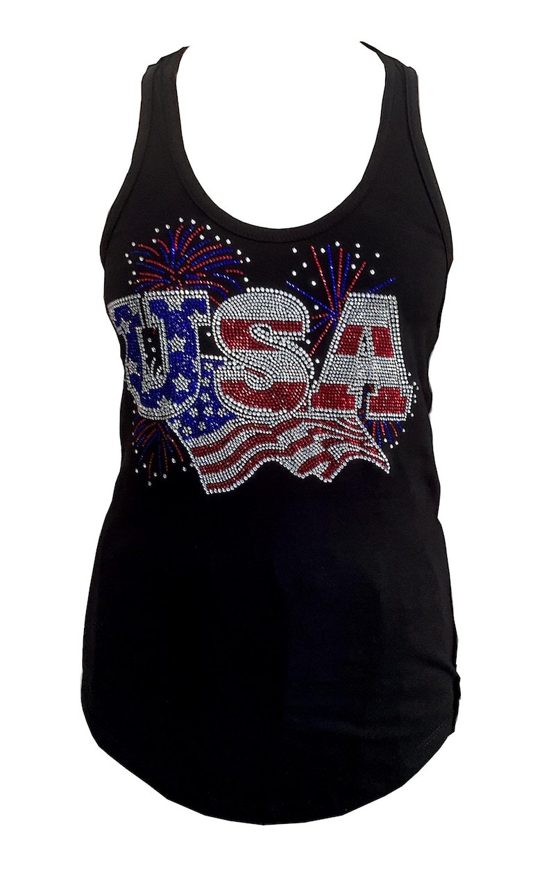 May include: Black tank top with the word "USA" in red, white, and blue rhinestones. The design includes a flag and fireworks. The tank top is sleeveless and has a scoop neck.