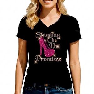 May include: A black V-neck t-shirt featuring a graphic design of a bright pink high-heeled shoe encrusted with sparkling rhinestones. The text "Standing On His Promises" is written in silver rhinestones above and below the shoe graphic.