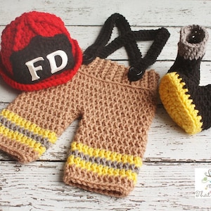 May include: Crocheted firefighter costume for a newborn baby. The outfit includes a red hat with the letters "FD" on the front, brown trousers with yellow and grey stripes, and black and yellow booties.