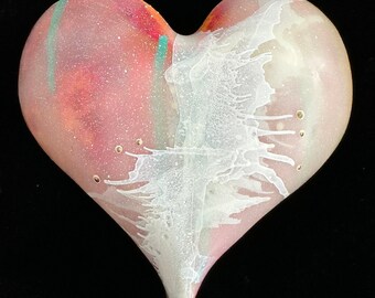 Puede incluir: Una escultura de vidrio en forma de corazón con un diseño de espiral rosa y blanco. El vidrio es translúcido y tiene una textura moteada.