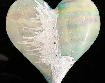 Puede incluir: Una escultura de vidrio en forma de corazón con un diseño de espiral blanco y verde. El vidrio es translúcido y tiene una textura moteada. Hay pequeños puntos dorados dispersos por toda la escultura.