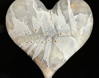Puede incluir: Una escultura de cerámica blanca en forma de corazón con una superficie texturizada y detalles dorados. El corazón tiene un esmalte blanco con un sutil acabado craquelado y un diseño abstracto único.