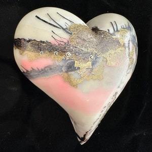 May include: A white heart-shaped glass ornament with pink, gold, and black abstract designs. The ornament has a glossy finish.