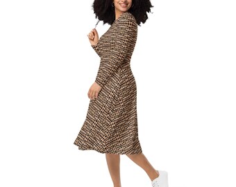 Puede incluir: Una mujer lleva un vestido midi de manga larga con un estampado geométrico negro y marrón. El vestido tiene un escote redondo y una falda ligeramente acampanada. Lleva zapatillas blancas.