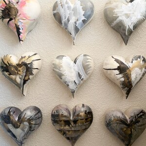 May include: Nine ceramic heart-shaped ornaments with a white base and black and gold abstract designs. The hearts are arranged in three rows of three.