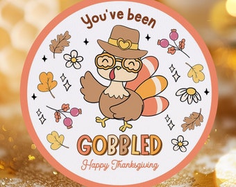May include: A round sticker with a cartoon turkey wearing glasses and a hat. The sticker says "You've been Gobbled Happy Thanksgiving".