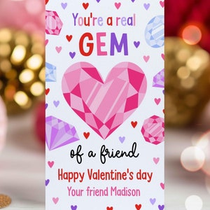 Puede incluir: Una tarjeta blanca con una gema rosa en forma de corazón en el centro. La tarjeta tiene el texto "You're a real GEM of a friend Happy Valentine's day Your friend Madison".