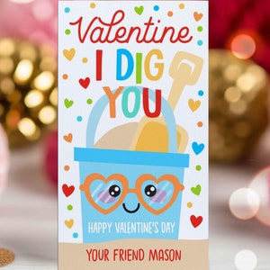 May include: A colorful Valentine's Day card with a blue bucket, a yellow shovel, and the text "Valentine I DIG YOU". The bucket has googly eyes and a happy face. The card also says "Happy Valentine's Day" and "Your Friend Mason".