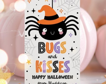 Può includere: Un'etichetta bianca con un ragno di cartone animato che indossa un cappello da strega. Il testo recita "Bugs and Kisses Happy Halloween from Maddigson".