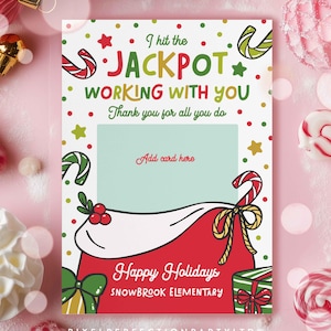 以下が含まれることがあります： 赤と白のデザインのホリデーをテーマにしたグリーティングカード。「I hit the JACKPOT WORKING WITH YOU」と「Happy Holidays」のテキストが特徴です。「Add card here」のスペースがあります。キャンディケインとギフトがカードを飾っています。
