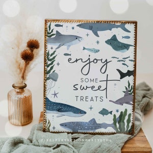以下が含まれることがあります： 金色の縁取りと「enjoy some sweet treats」の文字が入った長方形のサイン。グレー、ブルー、グリーンの色合いで、様々なサメ、魚、海洋生物のイラストが描かれています。