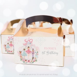 Puede incluir: Una caja de regalo rosa y blanca con un diseño de bailarina y cascanueces. La caja tiene un asa dorada y dice "Eloise's 1st Birthday".