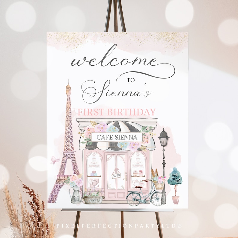 May include: A pink and white welcome sign for a first birthday party with a Parisian theme. The sign features a cartoon illustration of the Eiffel Tower, a cafe, and a bicycle with flowers. The text on the sign reads "Welcome to Sienna's First Birthday".