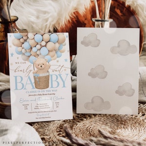 Peut inclure: Une invitation de f&ecirc;te pr&eacute;natale avec un ballon &agrave; air chaud en forme de ballon bleu et beige avec un ours en peluche dans un panier. Le texte dit "We can barely wait Baby Clarke is on the way".