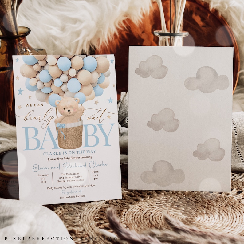 Peut inclure: Une invitation de f&ecirc;te pr&eacute;natale avec un ballon &agrave; air chaud en forme de ballon bleu et beige avec un ours en peluche dans un panier. Le texte dit "We can barely wait Baby Clarke is on the way".