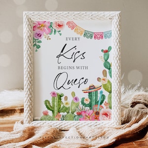May include: A white framed sign with a cactus and floral design. The sign reads "Every Kiss Begins With Queso".
