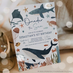 May include: A blue and white invitation card with a nautical theme. The card features a whale, a shark, a jellyfish, and other sea creatures. The text on the card reads "Oneder the Sea" and "Sebastian's 1st Birthday".