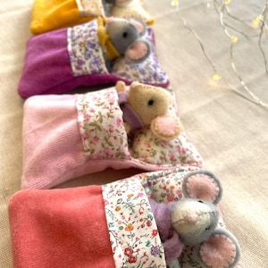 May include: A stack of handmade felt mice in colorful sleeping bags. The mice are gray with pink ears and are nestled in plush bags of yellow, purple, pink, and coral. The bags have floral patterned trim.