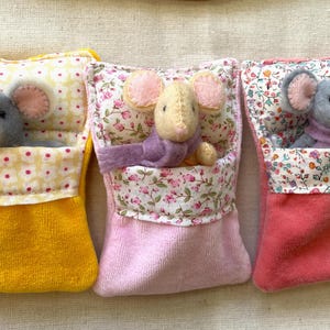 May include: Three handmade felt mouse toys nestled in colorful beds. The beds are in yellow, pink, and coral, with floral and polka dot patterns. Each mouse has large ears and a small scarf.