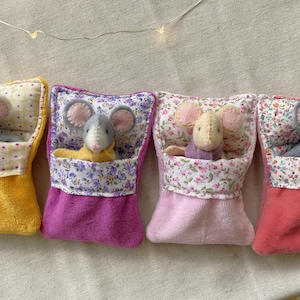 May include: Four handmade felt mice nestled in colorful fabric pouches. Each mouse has gray or tan fur and pink ears. The pouches are yellow, purple, pink, and red, with floral patterned tops. A whimsical, handcrafted item.