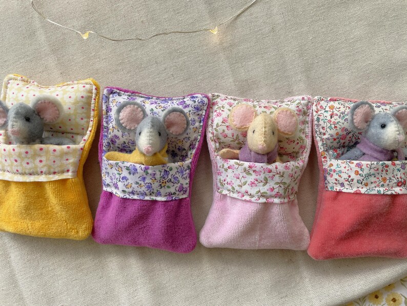 May include: Four handmade felt mice nestled in colorful fabric pouches. Each mouse has gray or tan fur and pink ears. The pouches are yellow, purple, pink, and red, with floral patterned tops. A whimsical, handcrafted item.