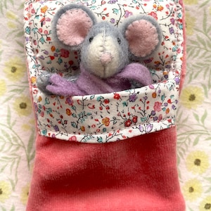 May include: A handmade plush mouse toy with gray fur, pink ears, and a lavender body, nestled in a pink velvet pouch. The pouch is lined with floral fabric in a variety of colors. The mouse is a charming, whimsical creation.