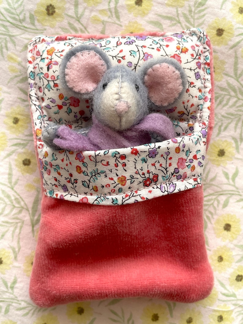 May include: A handmade plush mouse toy with gray fur, pink ears, and a lavender body, nestled in a pink velvet pouch. The pouch is lined with floral fabric in a variety of colors. The mouse is a charming, whimsical creation.