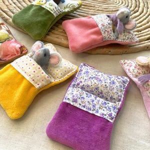 May include: A collection of handmade miniature beds with plush mice. The beds are in various colors, including yellow, pink, green, and purple, with floral patterned pillows and bedding. The mice are gray and beige.