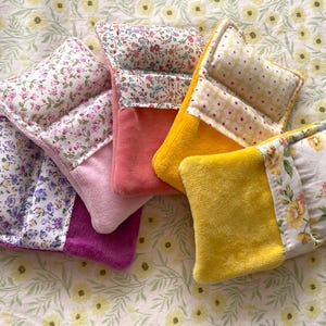 May include: A collection of colorful, floral-patterned fabric items. The items feature a combination of floral prints and solid colors, including pink, purple, and yellow. The items are likely small, decorative pillows or sachets.