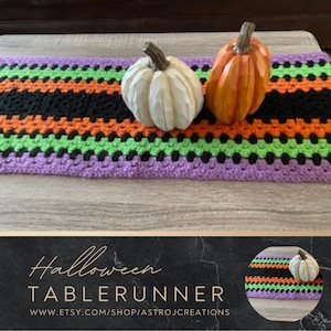 May include: A purple, green, orange and black crocheted table runner with two decorative pumpkins on top. The table runner has a striped pattern. The text "Halloween Table Runner" and "www.etsy.com/shop/astrojcreations" is displayed below the image.