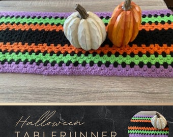 May include: A purple, green, orange, and black crocheted table runner with two decorative pumpkins on top. The table runner has a striped pattern. The text "Halloween Table Runner" and "www.etsy.com/shop/astrojcreations" is displayed below the image.