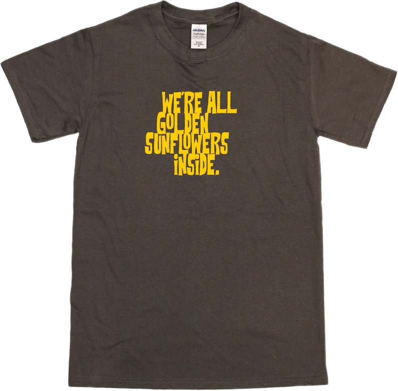 Puede incluir: Una camiseta gris oscuro con el texto "We're all golden sunflowers inside." impreso en amarillo.