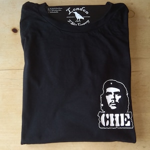 May include: Black t-shirt with a white Che Guevara graphic and the word "CHE". The label reads "London T-Shirt Company". The shirt is folded. The background is a wooden surface.
