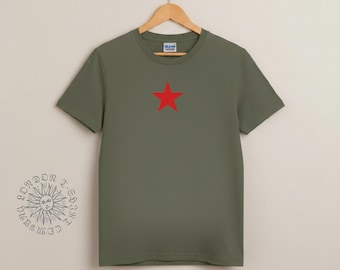 May include: Olive green t-shirt with a red star graphic centered on the chest. The short-sleeved shirt is hanging on a wooden hanger against a neutral background. The Gildan logo is visible on the collar.