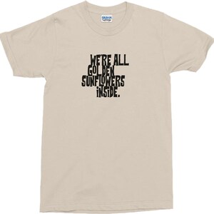 Puede incluir: Una camiseta beige con texto negro que dice "We're all golden sunflowers inside."