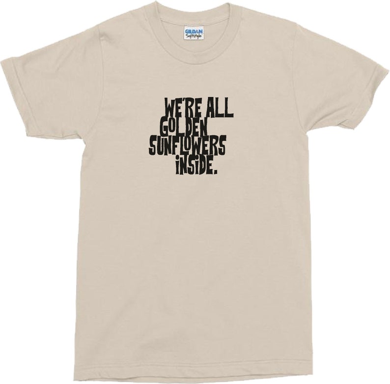 Puede incluir: Una camiseta beige con texto negro que dice "We're all golden sunflowers inside."