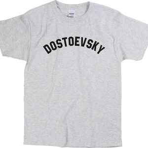 K&ouml;nnte beinhalten: Ein graues T-Shirt mit schwarzem Text, der "DOSTOEVSKY" in einer gew&ouml;lbten Schriftart lautet.
