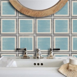 May include: A bathroom with a white porcelain sink and three chrome taps. The wall behind the sink is tiled with light blue and grey square tiles.