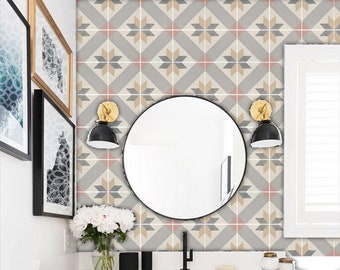 Può includere: Un bagno con un piano di lavoro bianco e un mobile da bagno nero. Il rivestimento a parete è un motivo geometrico di piastrelle grigie, beige e rosa. Uno specchio rotondo è appeso sopra il lavandino e ci sono due applique da parete nere con dettagli dorati su entrambi i lati dello specchio.