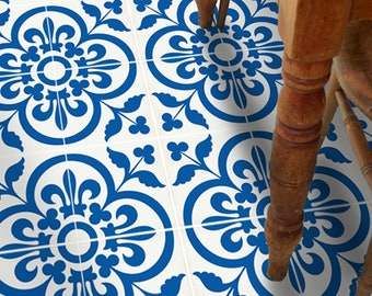 Puede incluir: Una serie de baldosas cuadradas para suelo con un patrón repetitivo de motivos florales y geométricos en azul intenso sobre un fondo blanco. Las baldosas están dispuestas en cuadrícula, con las patas de una silla de madera visibles arriba.
