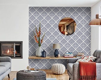 May include: A living room with a gray couch, a gray ottoman, and a gray armchair. The wall behind the furniture is covered in a blue and white geometric wallpaper. There is a fireplace with a wood mantle and a wood-burning fire. There is a wooden shelf with a vase of flowers, a lamp, and books.