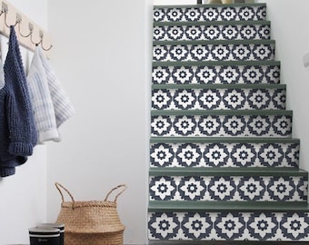 May include: A set of stairs with a black and white geometric pattern on the risers. The stairs are painted a dark green color. The stairs are in a hallway with a white wall and a wooden coat rack with a brown leather backpack and blue and white sweaters hanging on it.