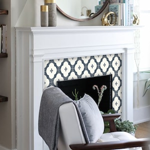 May include: A white fireplace mantel with a blue and white patterned tile surround. A grey throw blanket and a white armchair are in front of the fireplace.