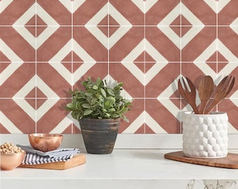 May include: A kitchen scene featuring a countertop with a geometric tile backsplash in terracotta and white. A small potted plant, copper bowl, and wooden utensils in a white textured holder are on the counter. The cabinet doors are gray.