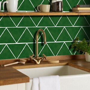 Puede incluir: Un fregadero de cocina con un grifo dorado y un salpicadero de azulejos verdes. Los azulejos están dispuestos en forma de espiga.