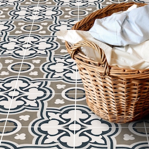 May include: A wicker laundry basket filled with white and blue clothing sits on a patterned floor with a geometric design in shades of grey, white, and blue.